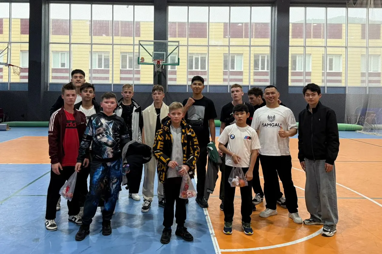 A group of boys in a sports hall with a man wearing a Samgau Bilim Foundation T-shirt.